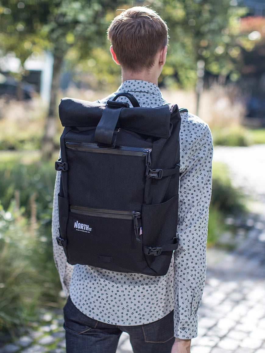 Guy walking in park wearing a black Flanders Backpack. | North St Bags - all-groups