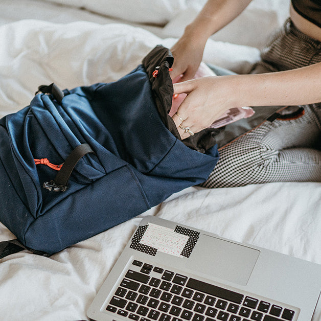 Woman on bed packing a backpack with a laptop. | North St Bags