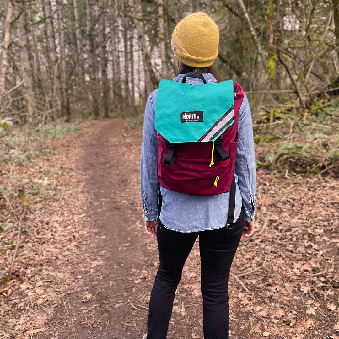 Woman wearing a red and teal backpack on a park trail. | North St Bags