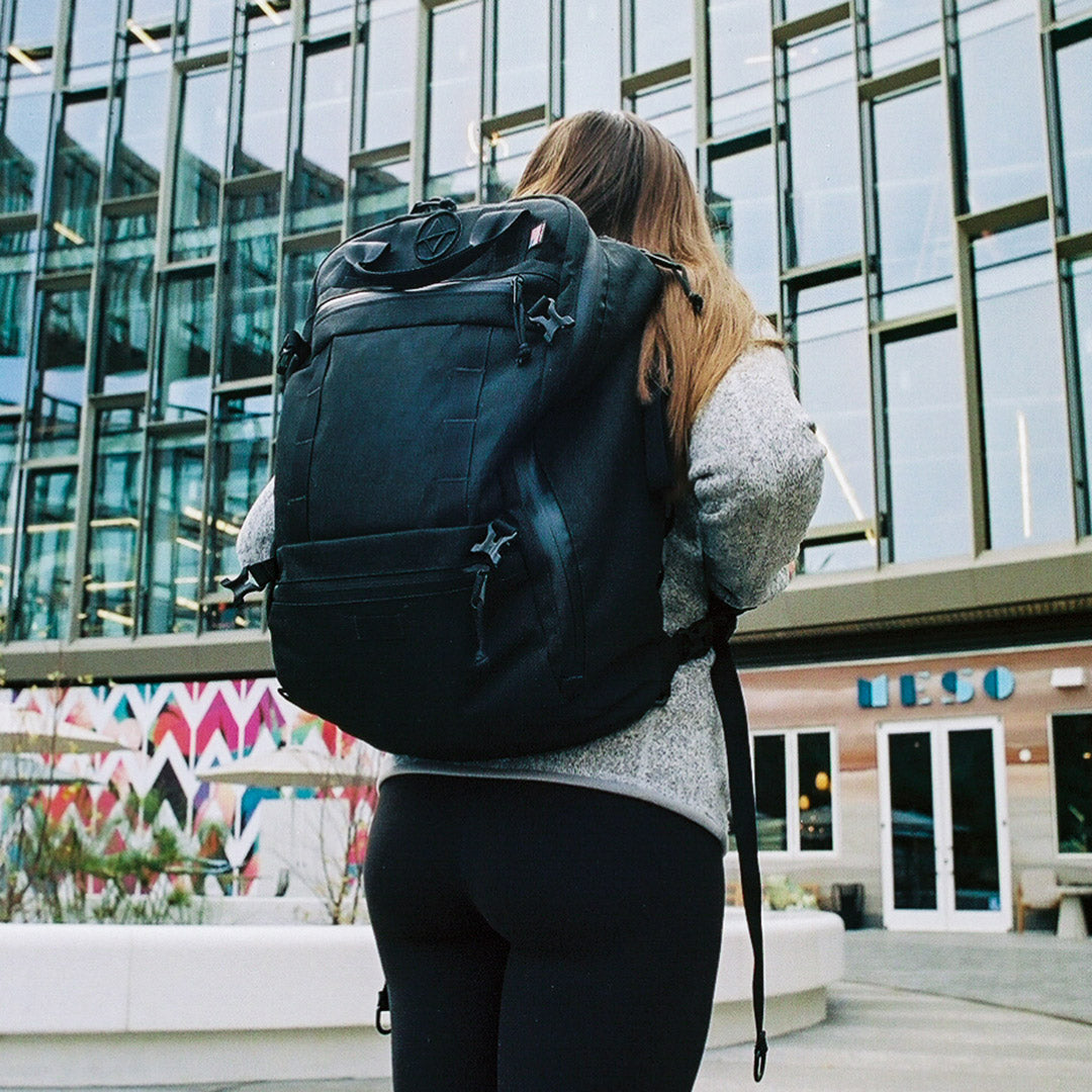 woman in in a city building plaza wearing a black travel backpack