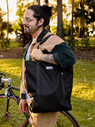 Man holding a black bag with 'The North Street' logo in a park setting