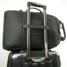 A black travel backpack with the backpack straps stowed and the luggage strap set onto a rolling luggage handle.